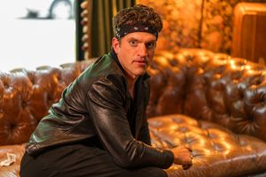 Person in leather jacket sitting on brown leather couch in well-lit interior.