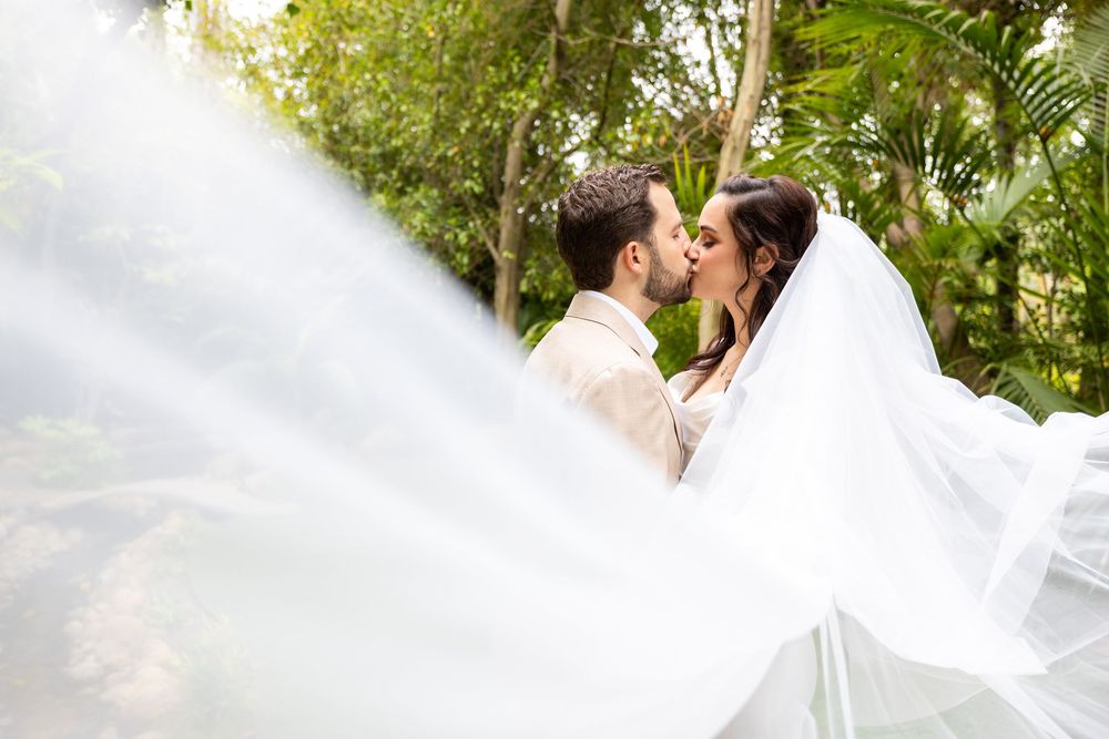 Wedding veil flowing in gentle breeze as a couple shares an intimate moment in a lush garden setting.
