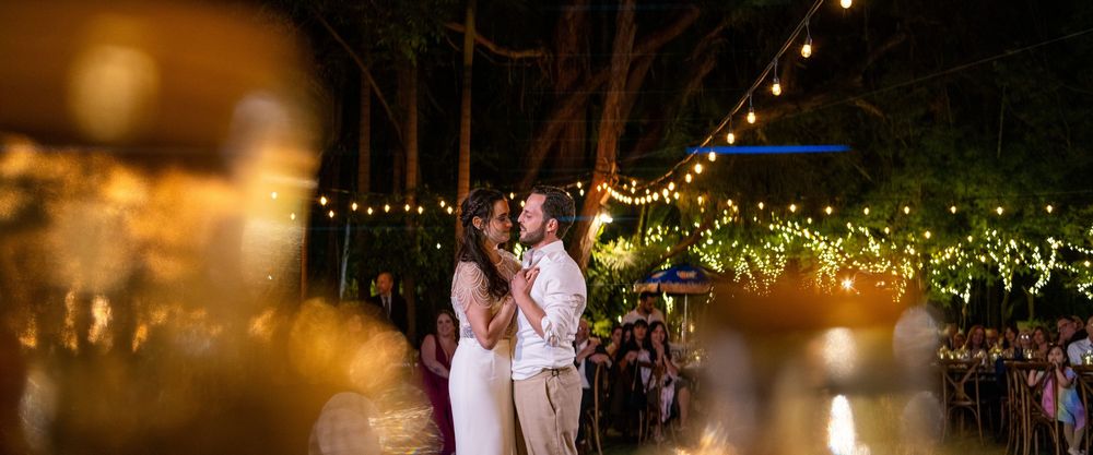 A couple dances together at an outdoor evening reception with string lights and greenery creating a romantic atmosphere.