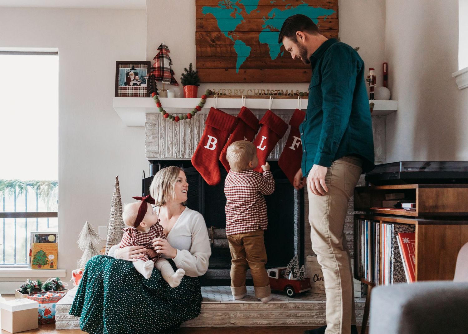 People sitting and standing in a cozy living room with wooden walls and bright natural lighting.