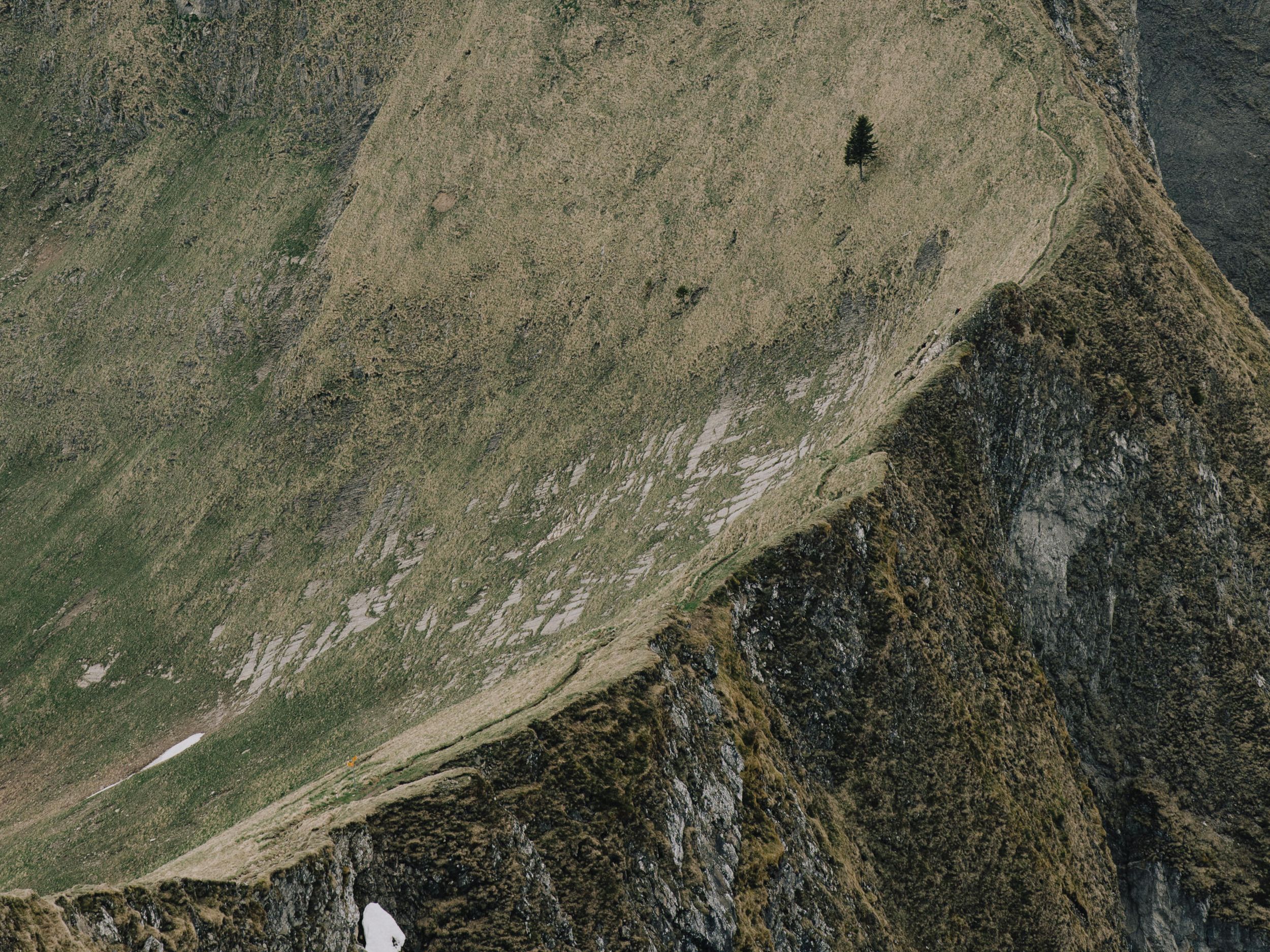 Aerial view of a rugged mountain slope with steep rocky terrain and sparse vegetation in remote wilderness.