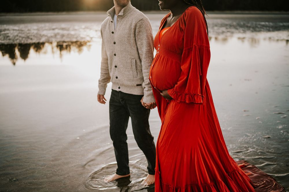 Maternity portrait of couple holding hands in water kye bay beach in red dress during sunset Comox Valley Vancouver Island photographer