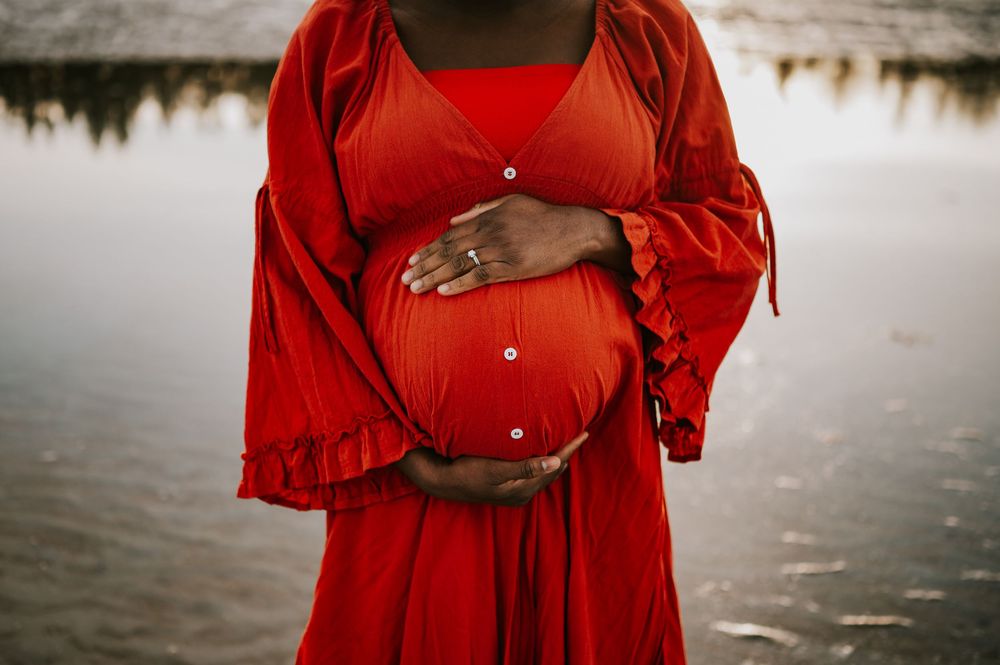 Maternity photoshoot of woman holding bump along kye bay beach in red dress during sunset Comox Valley Vancouver Island photographer
