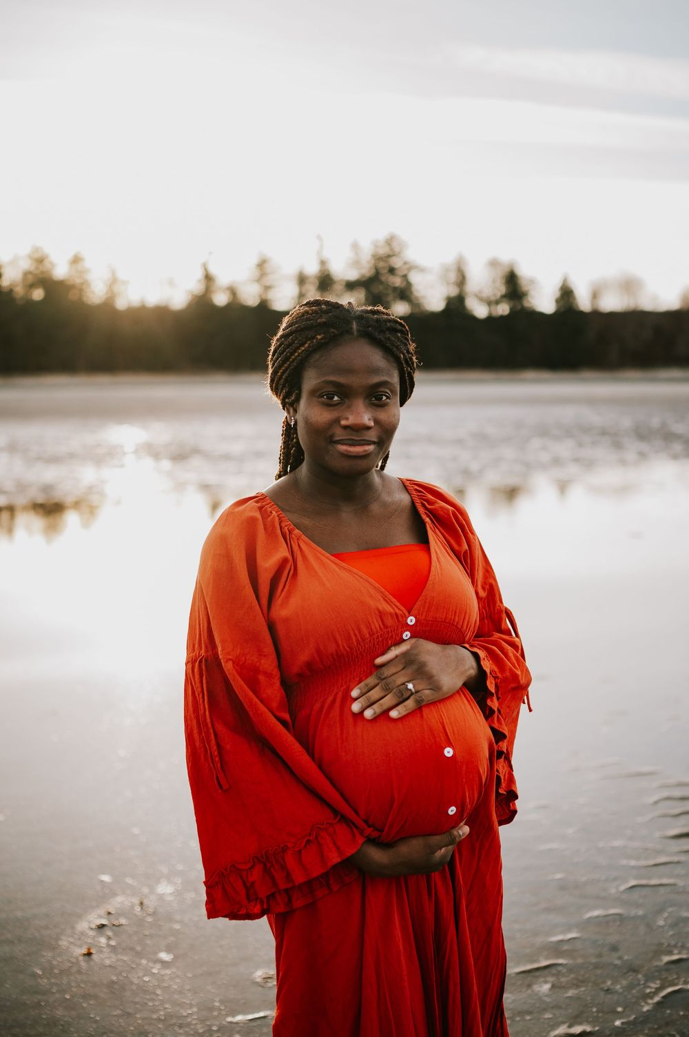 Maternity portrait of woman holding bump along kye bay beach in red dress during sunset Comox Valley Vancouver Island photographer