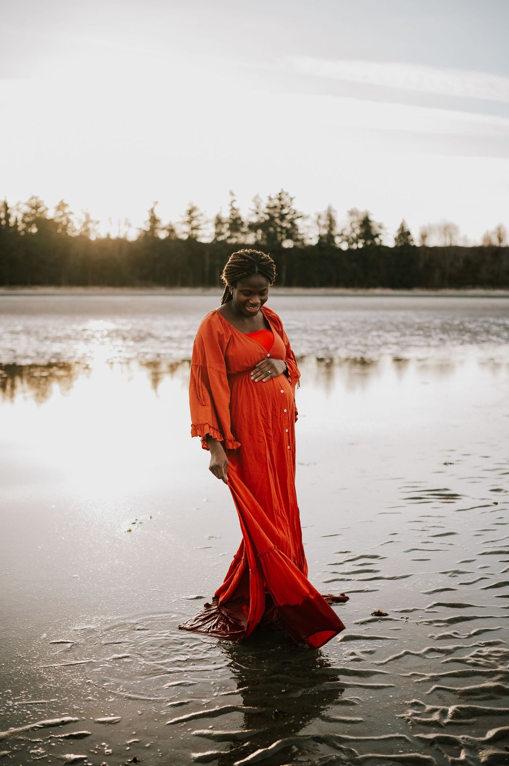 Maternity portrait of woman holding bump along kye bay beach in red dress during sunset Comox Valley Vancouver Island photographer