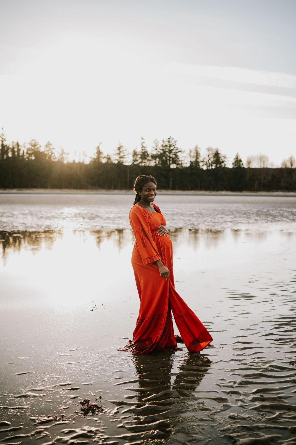 Maternity portrait of woman holding bump along kye bay beach in red dress during sunset Comox Valley Vancouver Island photographer