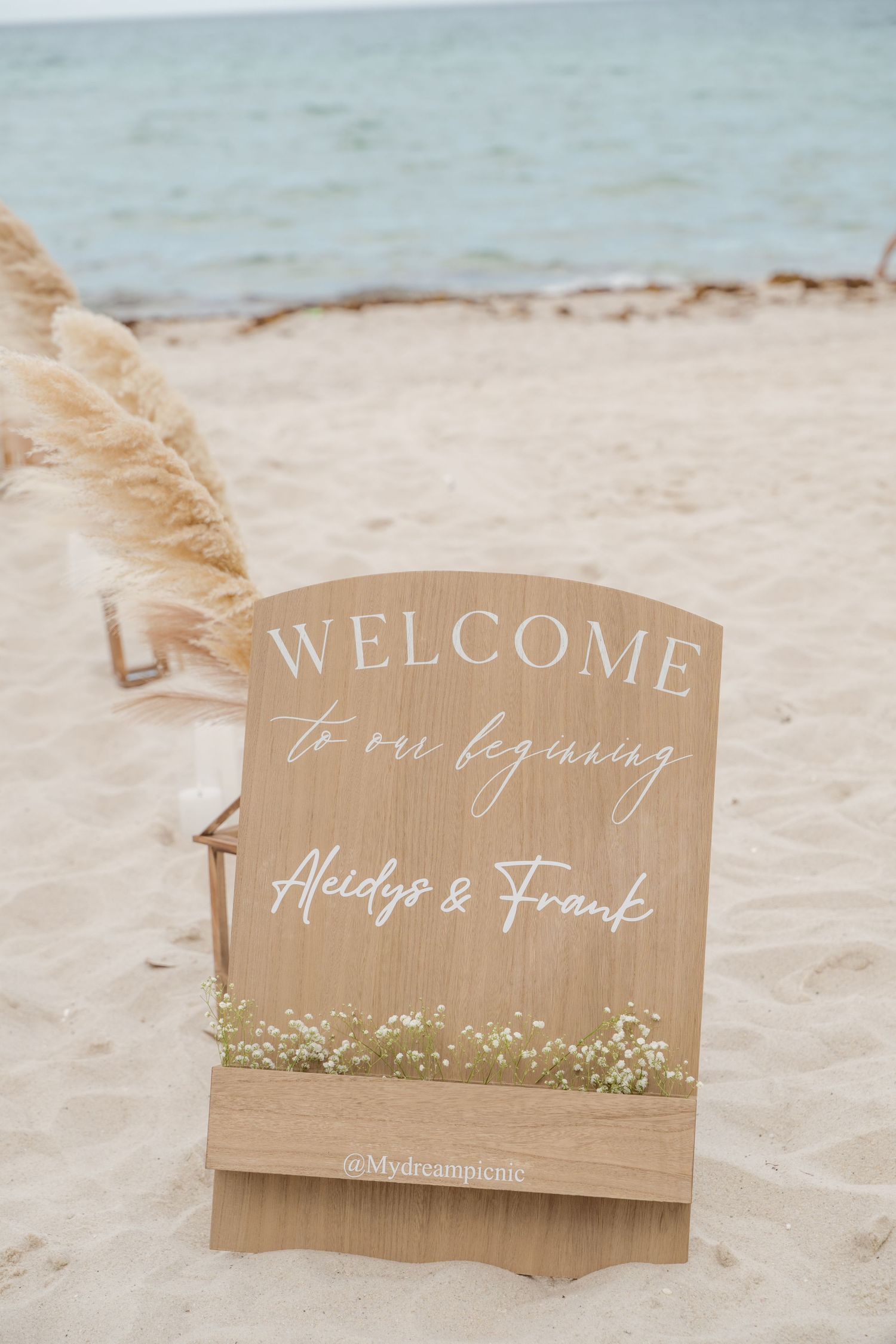 Brown wooden wedding welcome signs displayed on a sandy beach with soft waves in the background.
