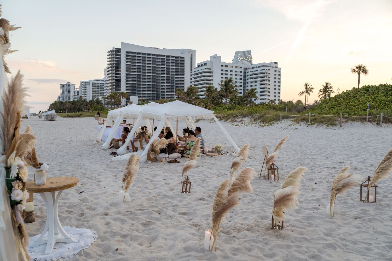 Bohemian beach wedding setup with pampas grass and white fabric tent on Miami Beach with luxury hotels in background.