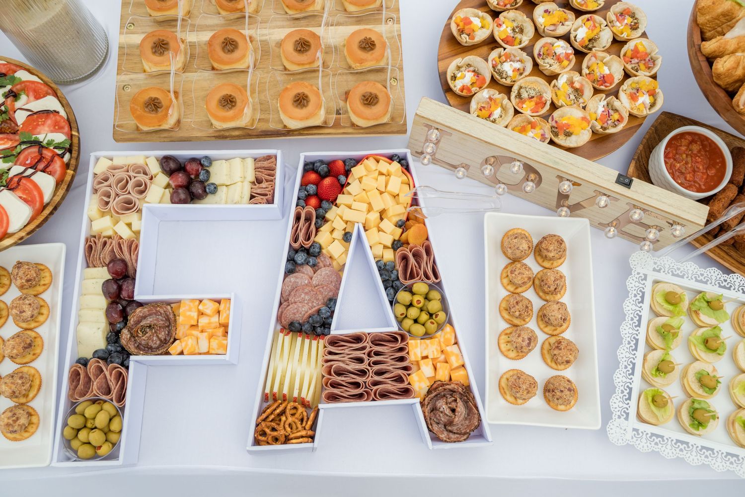 A catering display of finger foods and appetizers arranged on a long white table with various hors d'oeuvres.