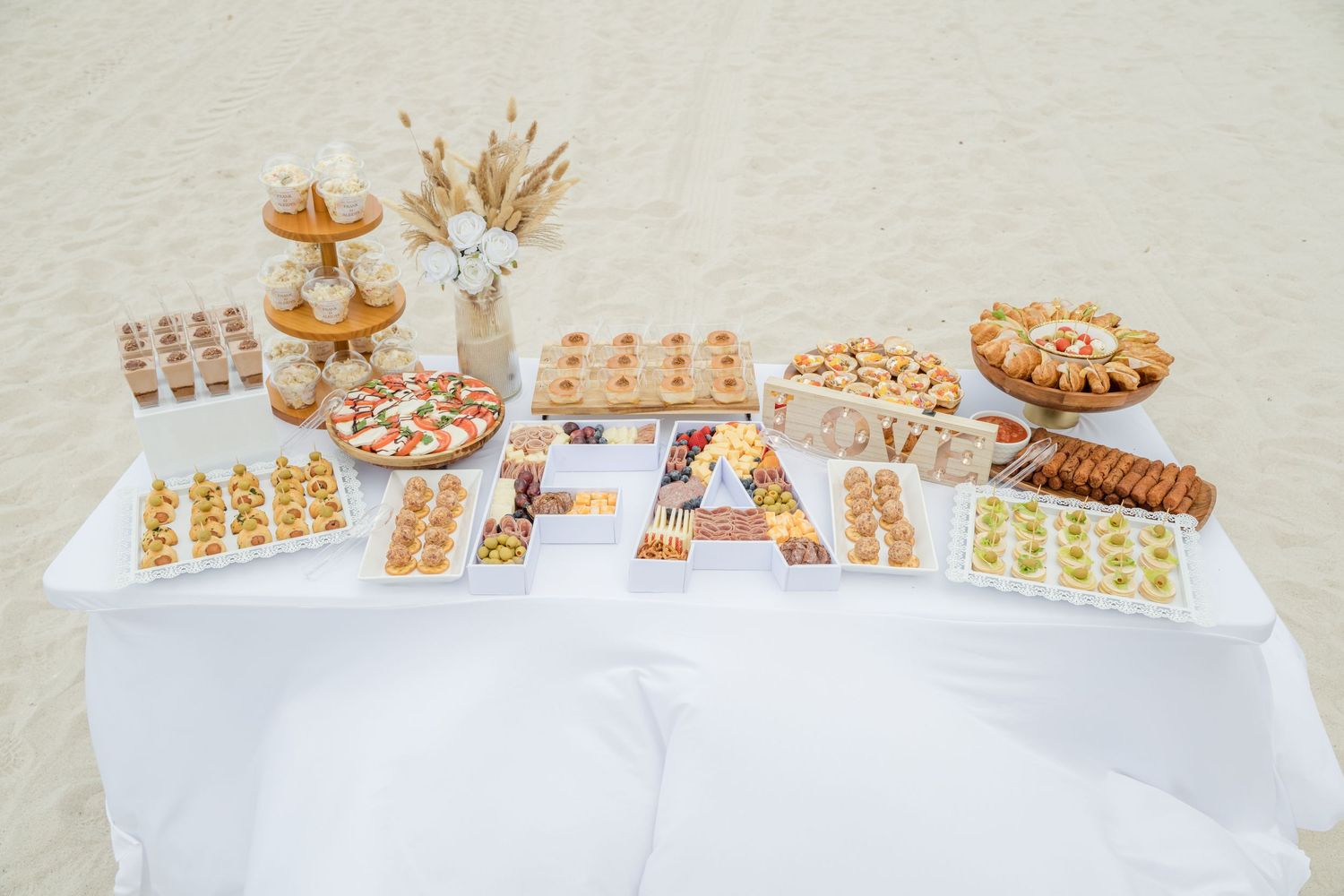 An elegant dessert table display with various pastries and sweets arranged on a white tablecloth with golden decorations.