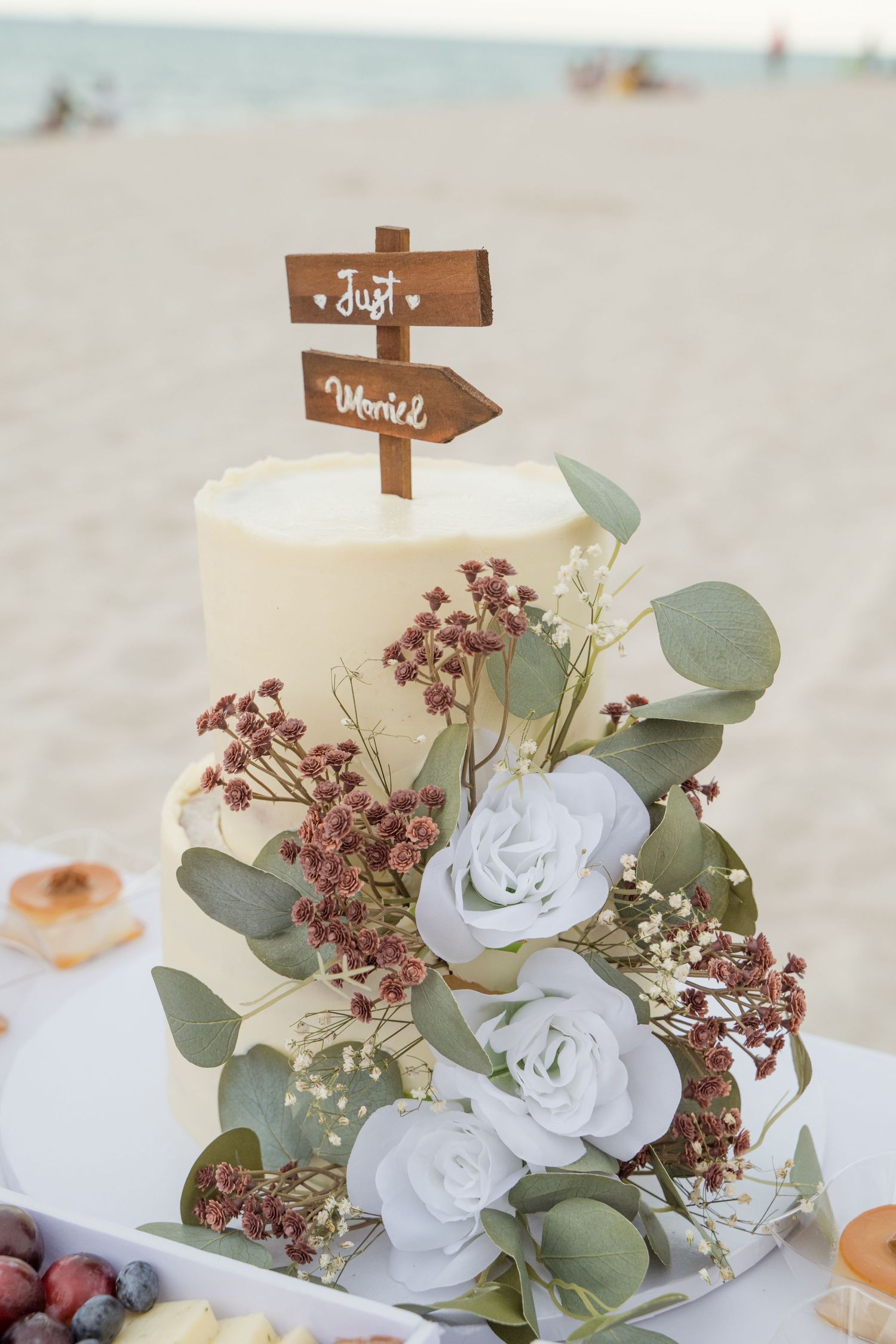 Elegant wedding table decor featuring white roses, eucalyptus leaves, and burgundy florals with wooden table number signs.