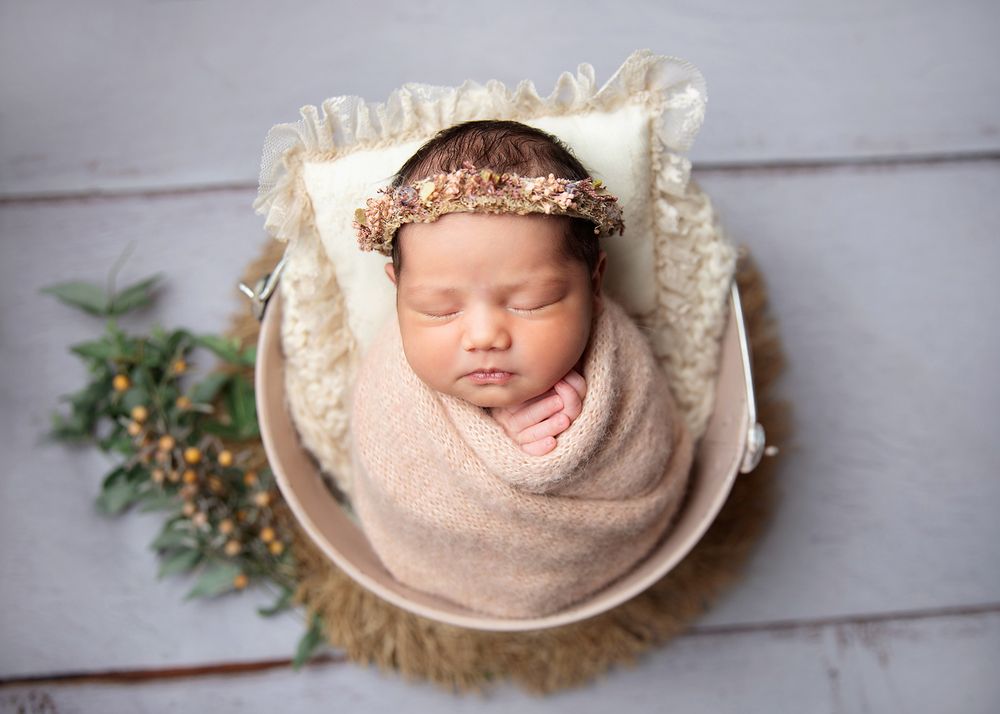 A newborn baby sleeps peacefully in cosy white wraps and bonnets across artistic photography poses. During a newborn session In London.