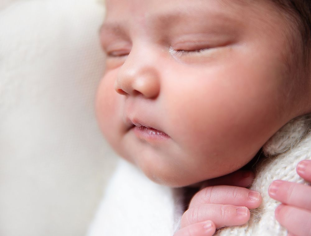 A sleeping newborn baby rests peacefully with closed eyes, wrapped in soft white and pink blankets. During a newborn session In London