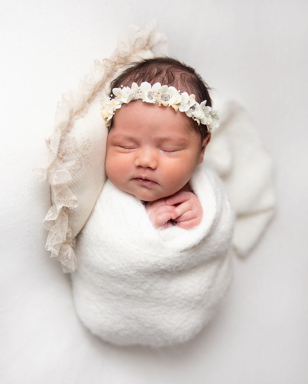 Sleeping newborn baby wrapped in white blanket photographed showing peaceful slumber. During a newborn session In London
