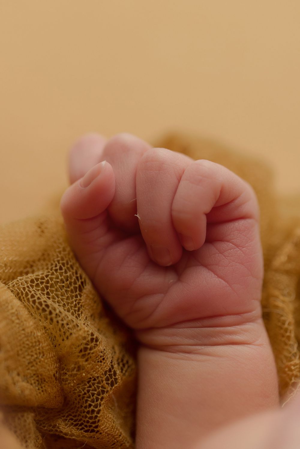 Close-up of a tiny newborn baby's clenched fist resting on golden fabric.