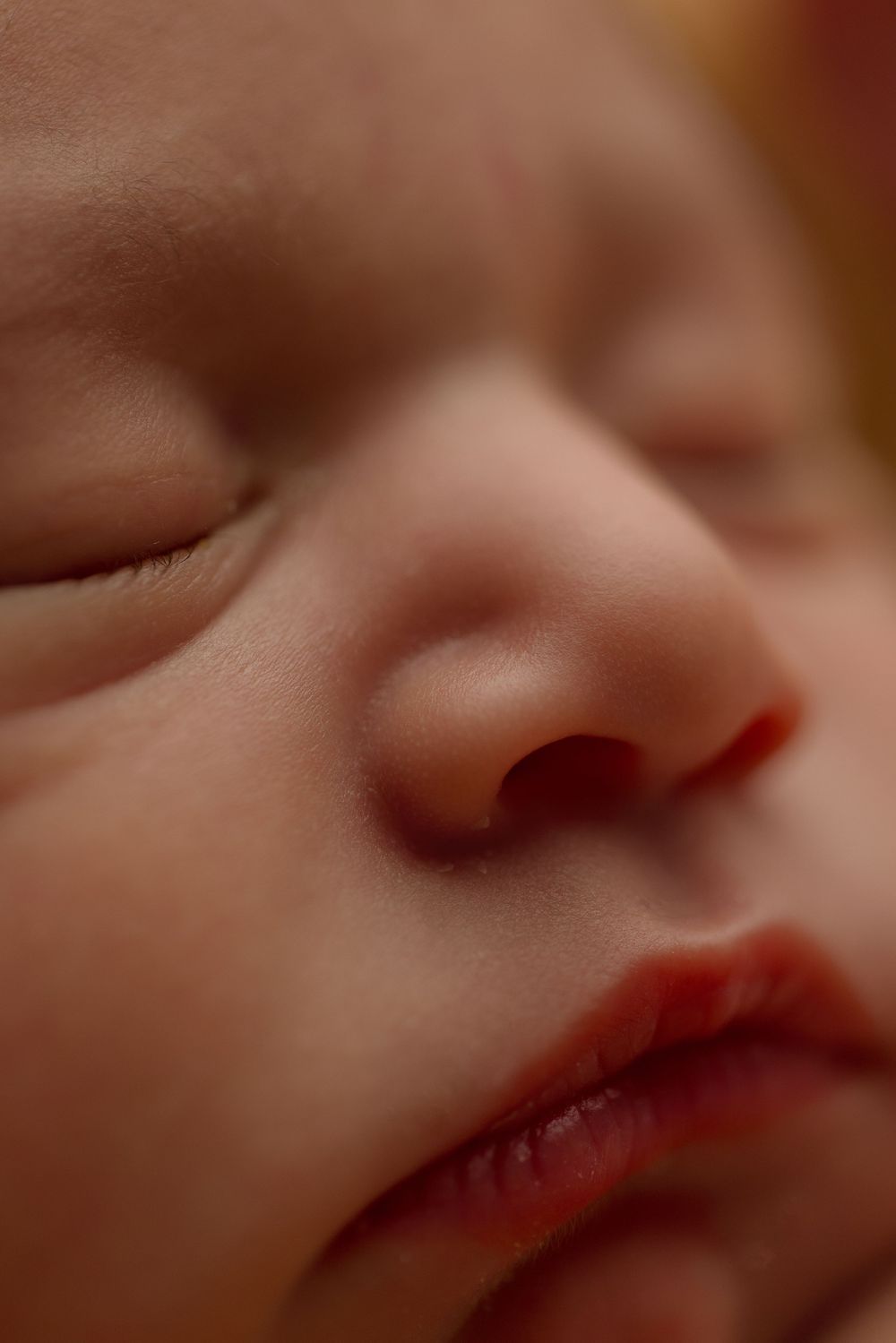 Close-up macro photograph of a peaceful sleeping child's face showing nose and lips in soft lighting.