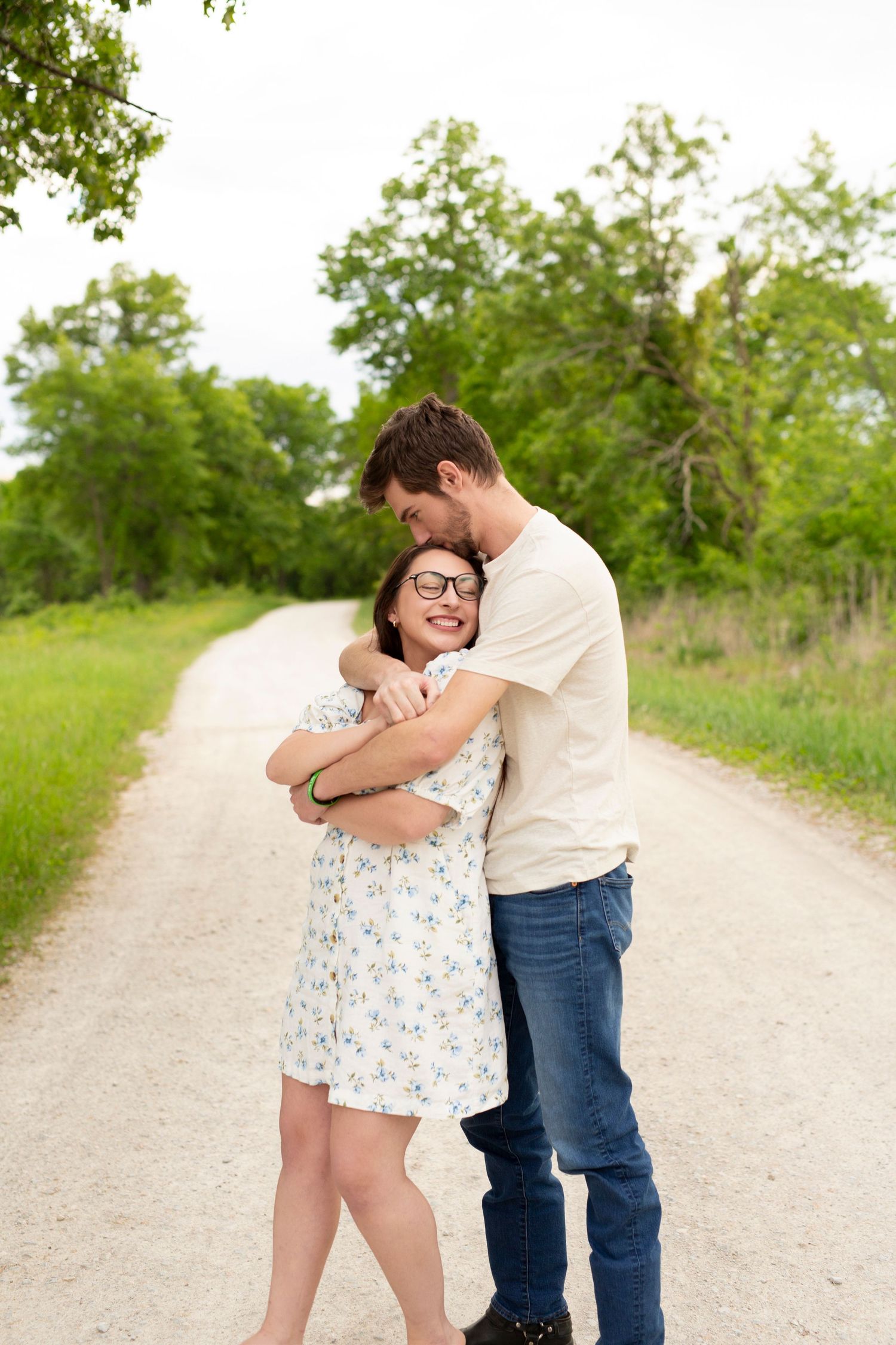 A couple embraces lovingly on a rural path with lush greenery in the background.