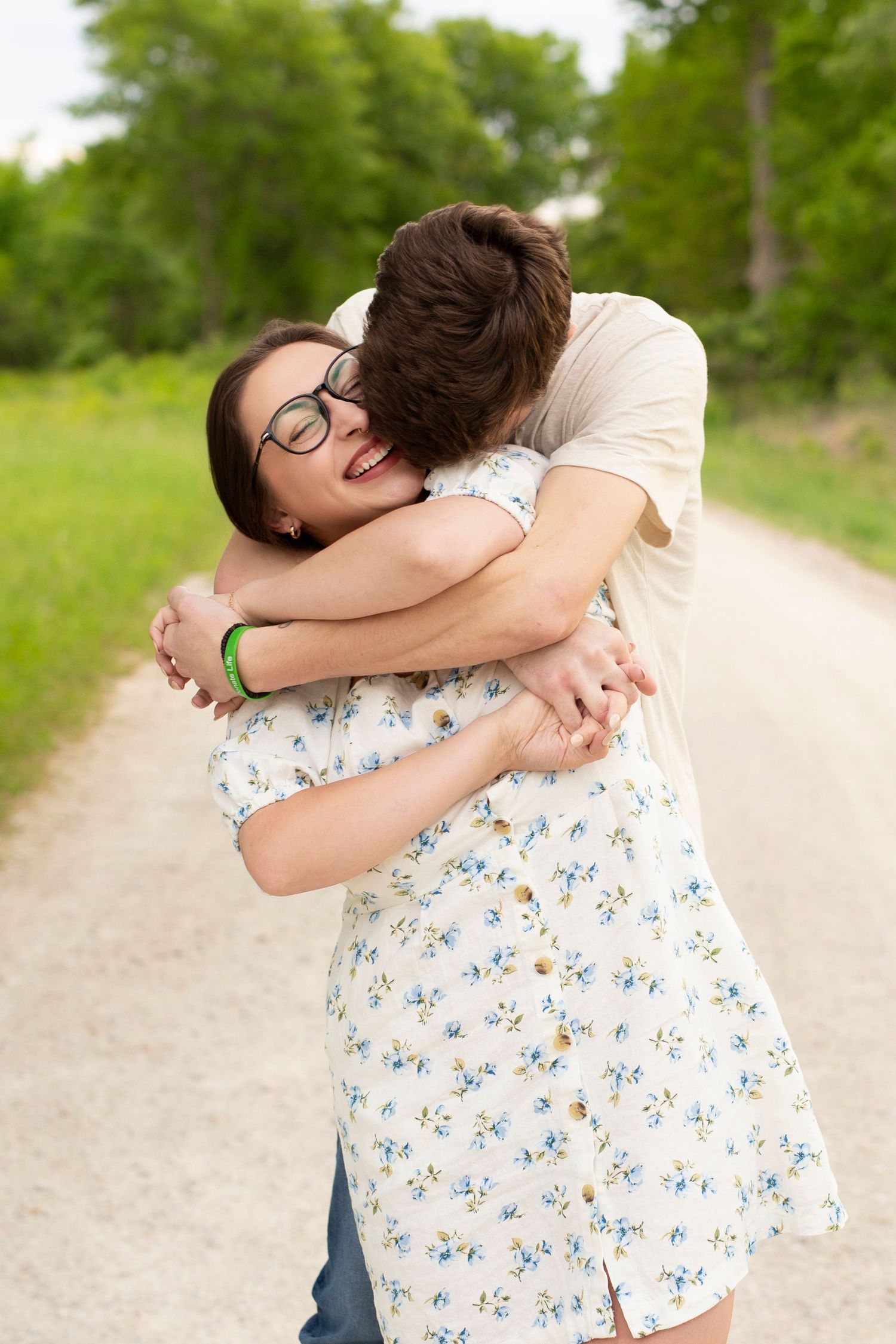 A couple in casual attire sharing a tender embrace on a gravel path with green foliage visible in the background.