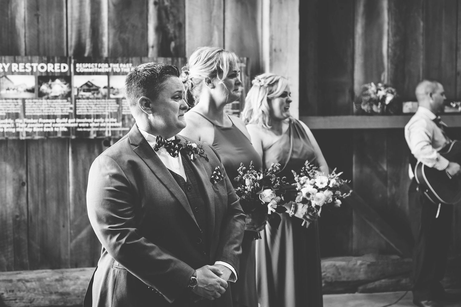 Black and white photo of an emotional moment between two people holding bouquets at a rustic wedding ceremony.