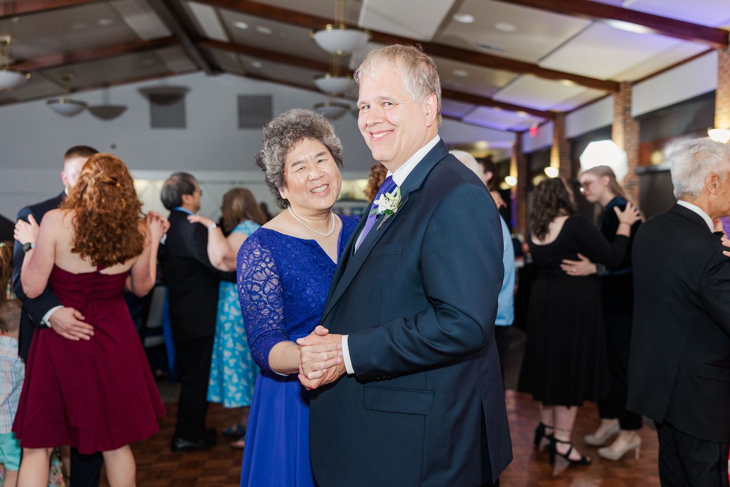 Elegant couple in blue dress and navy suit dancing at a formal event reception.