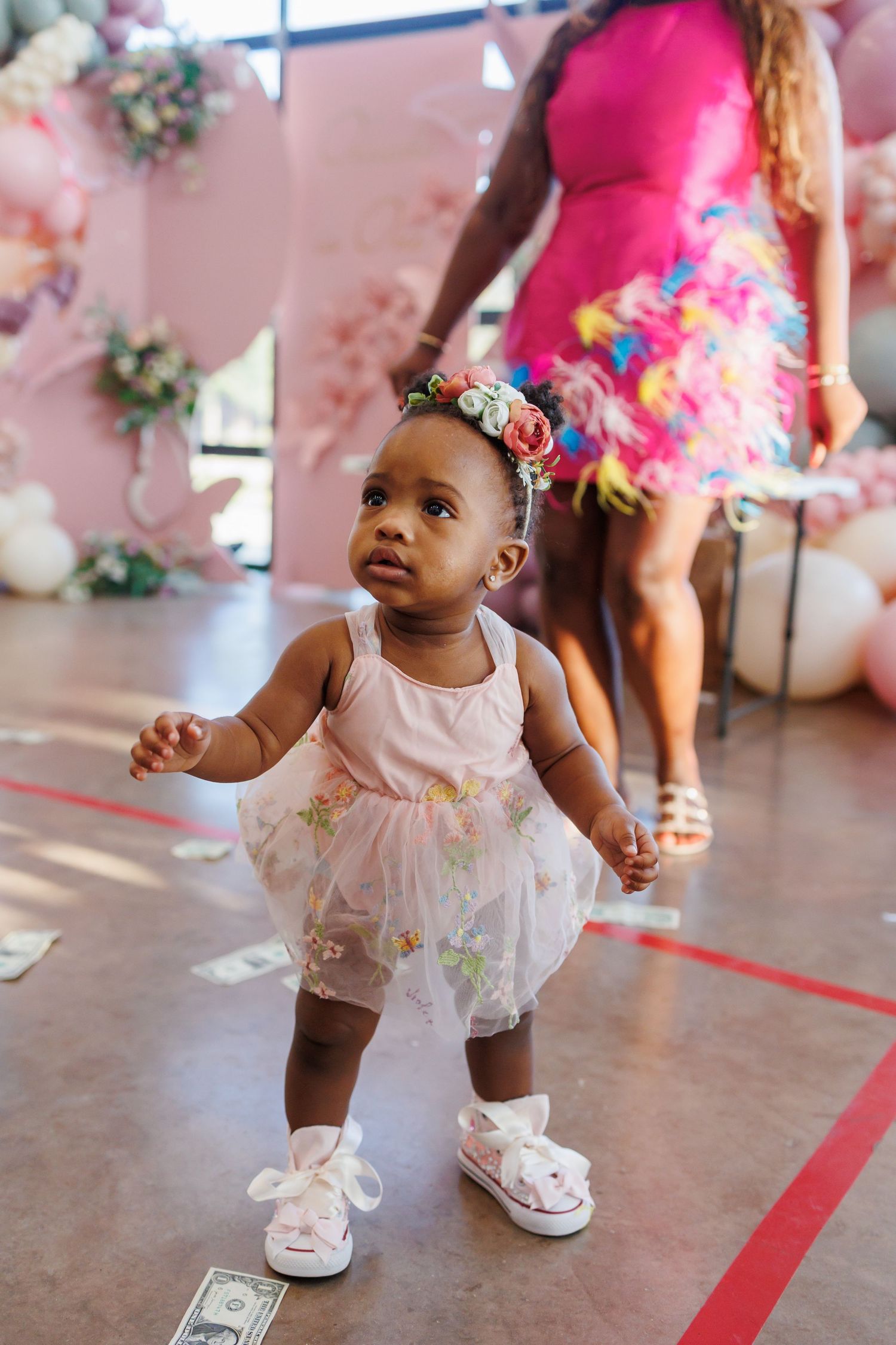 One-year-old girl in pink tulle dress and sneakers dances at her birthday party in a pink tulle dress and custom bedazzled sneakers