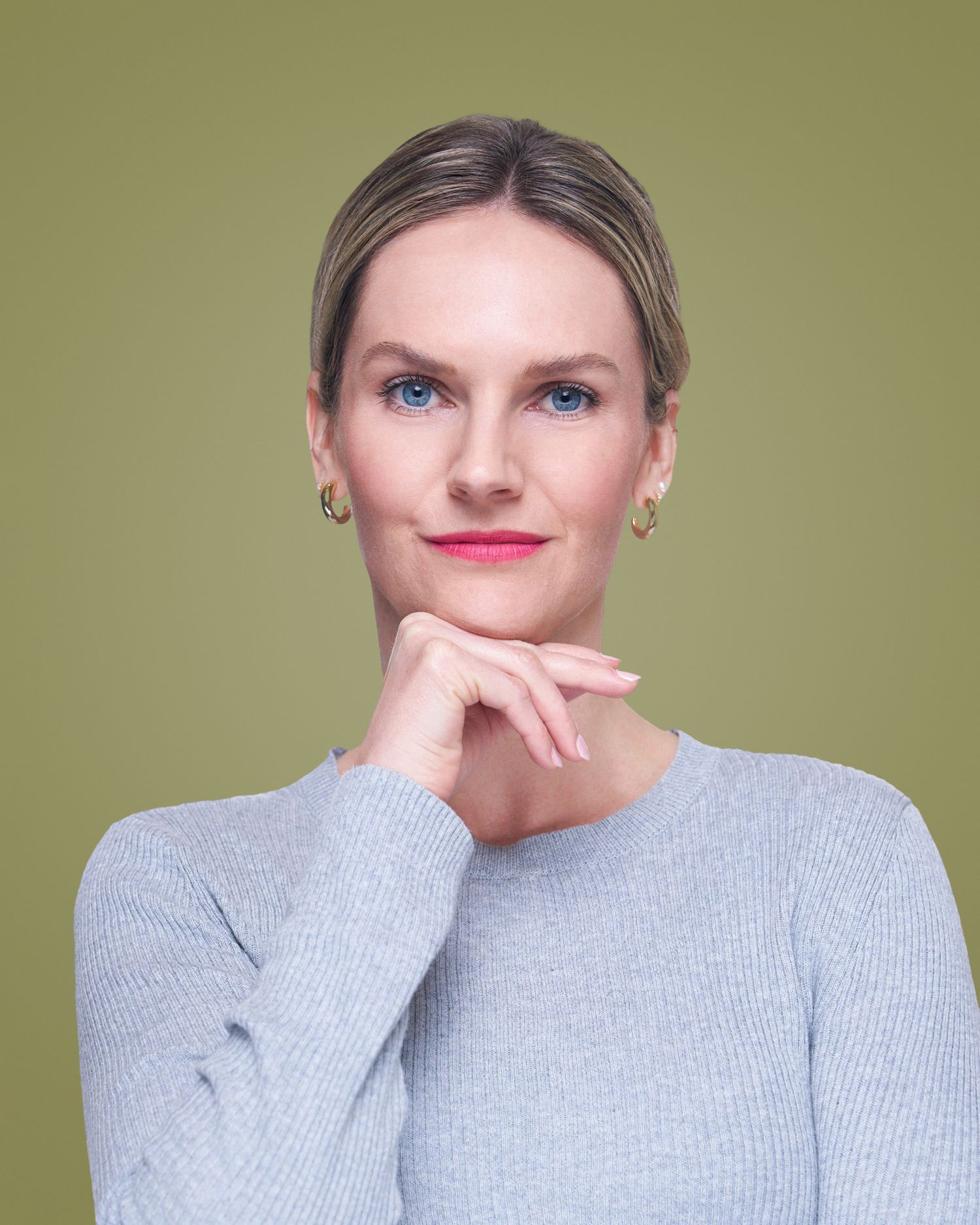 Professional headshot with gray sweater against olive green background.