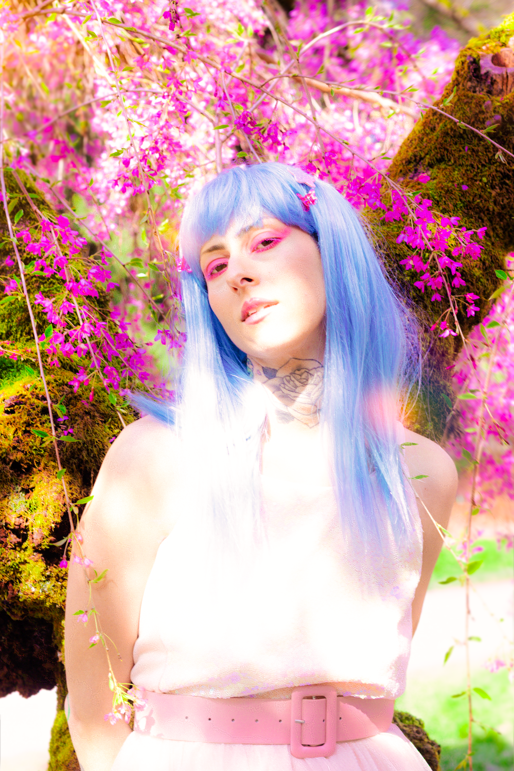 An ethereal portrait amidst pink cherry blossoms featuring blue hair and soft pastel styling.
