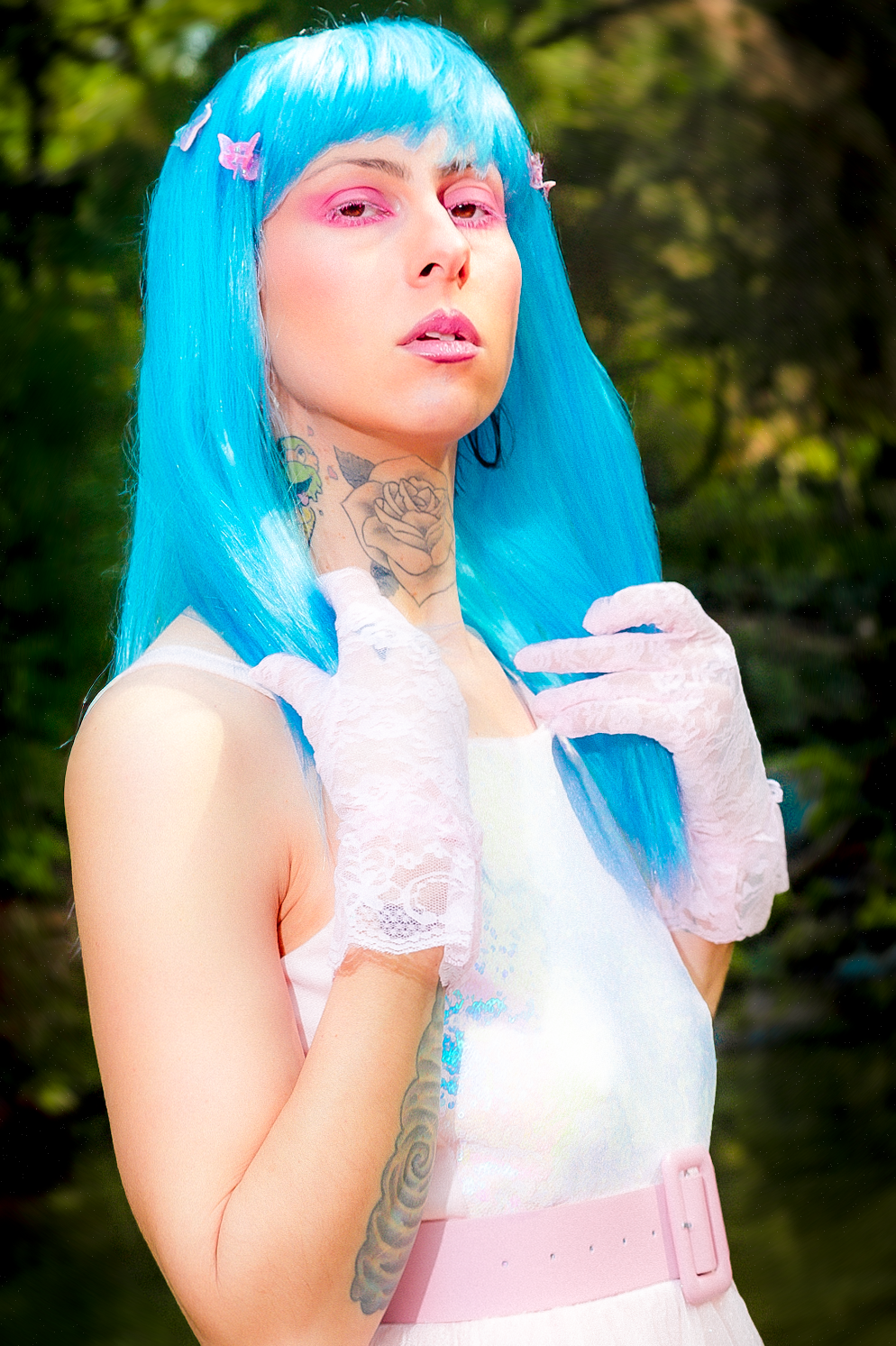 A cosplay portrait featuring bright blue long hair, white lace gloves, and a pink and white outfit in an outdoor setting.