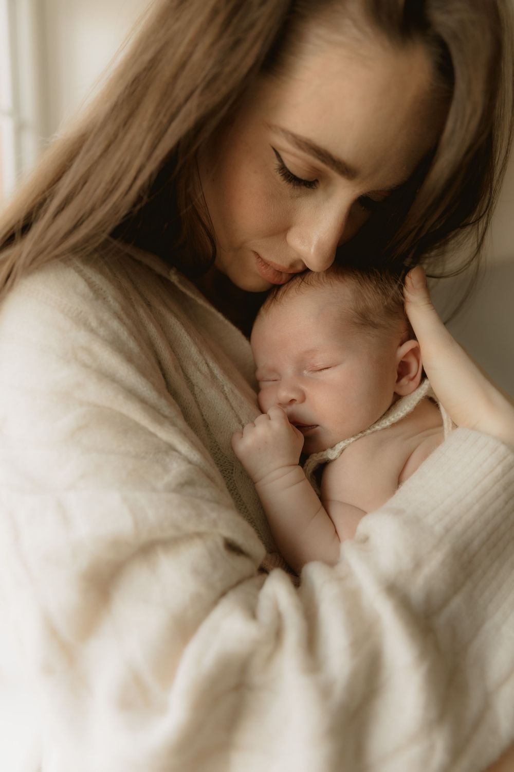 A tender moment between parent and sleeping newborn baby cuddled together in cozy white sweaters.