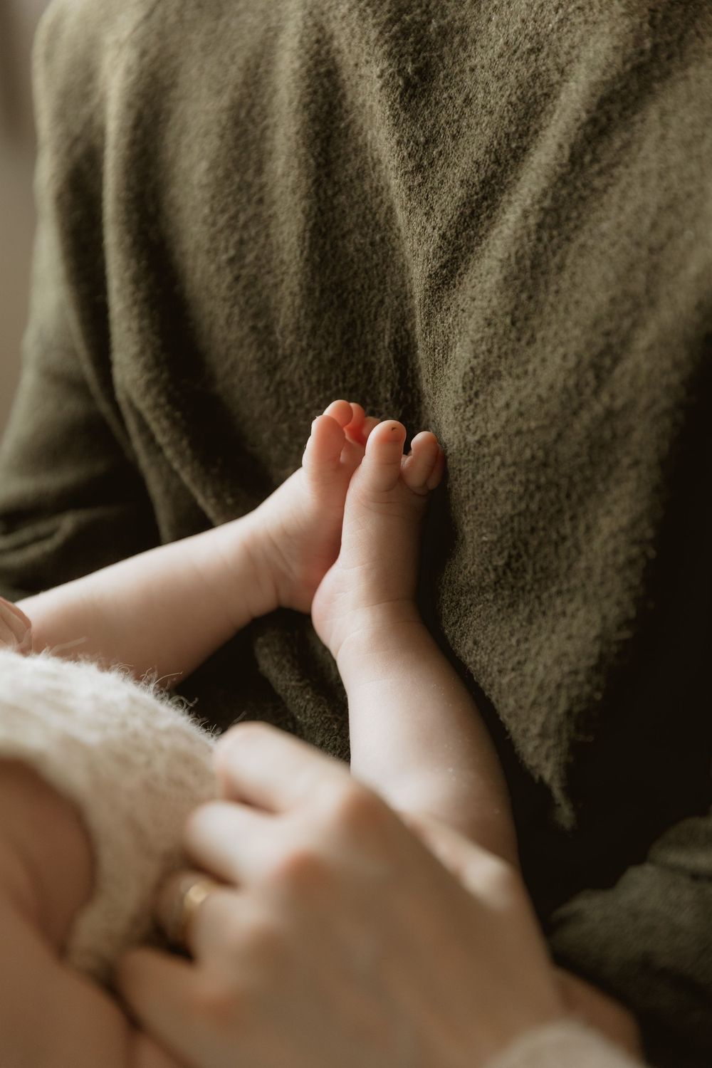 Close-up view of tiny baby toes against a dark olive green blanket in soft natural light.