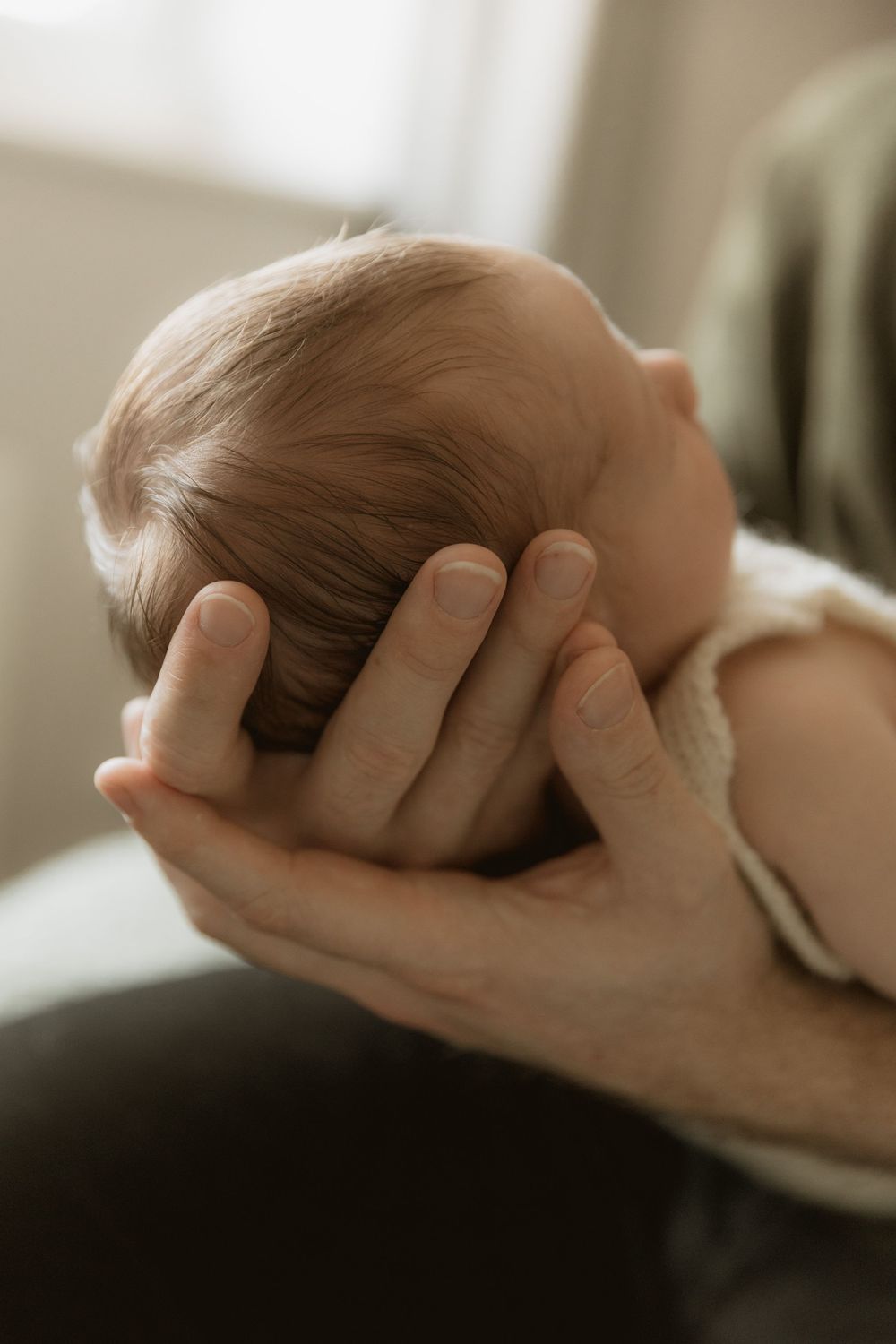 Adult hands gently cradle a baby's head in soft, warm lighting.