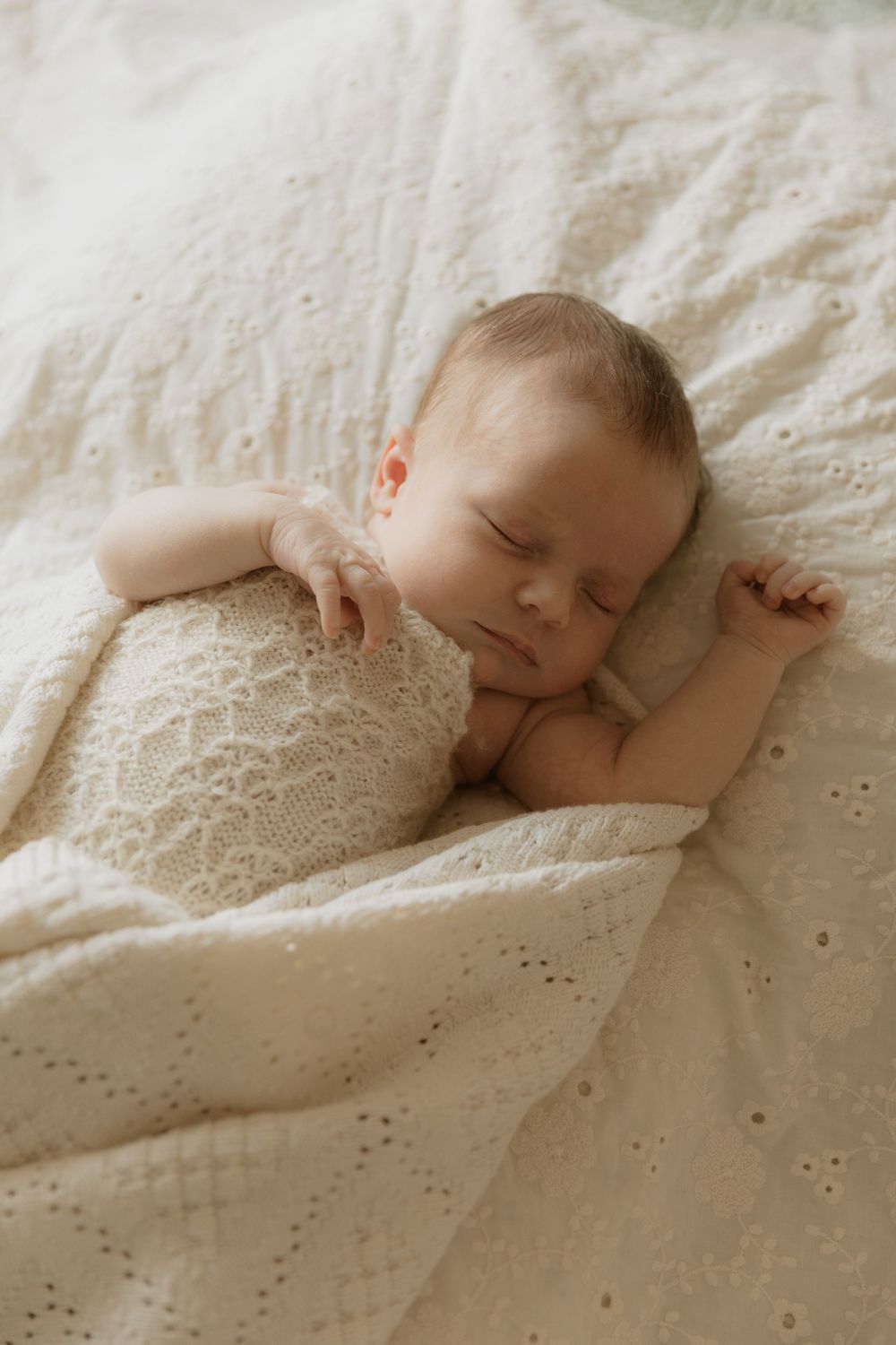 Sleeping infant peacefully resting on white textured bedding with delicate eyelet pattern.