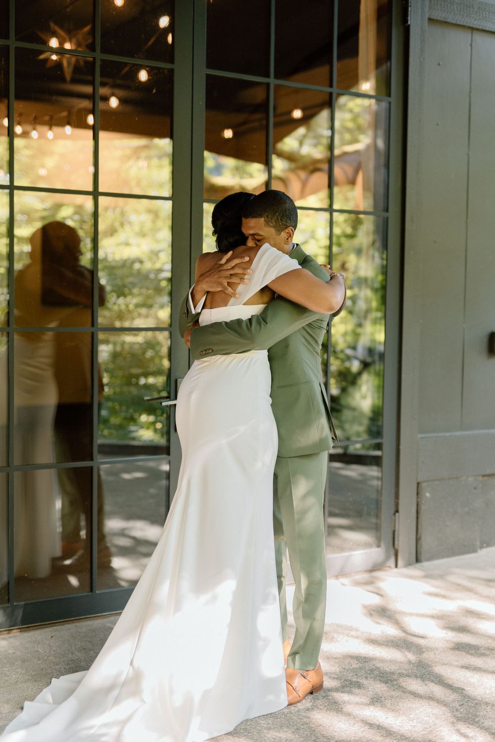 A romantic embrace between newlyweds, with the bride in white and the groom in a sage green suit.