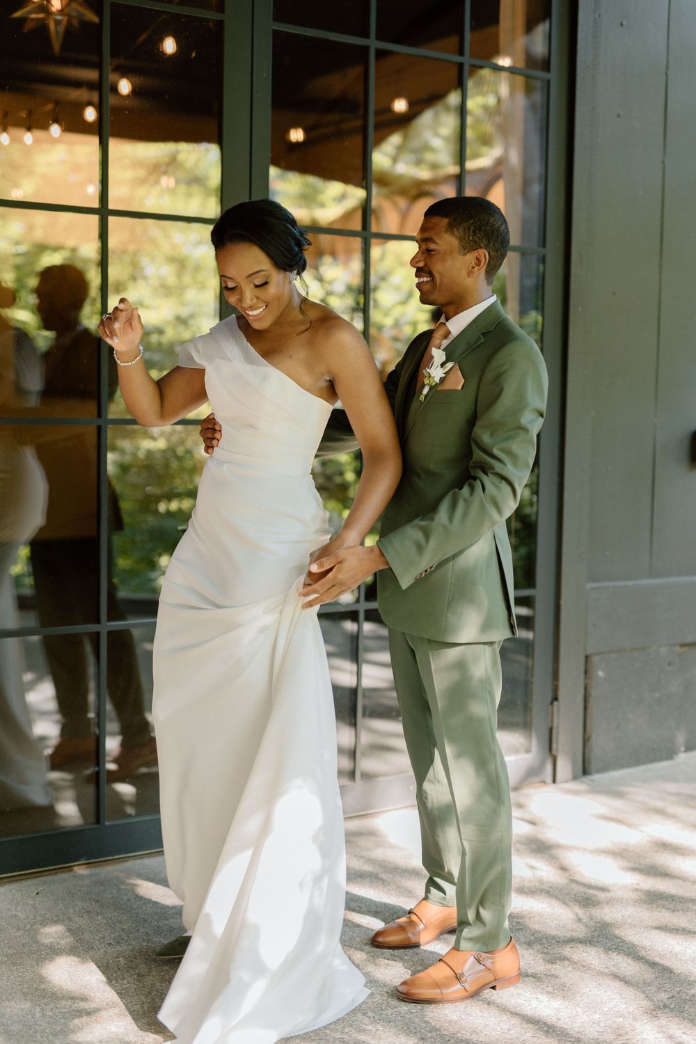 A joyful couple dancing together at their wedding, with the bride in a white gown and groom in a sage green suit.
