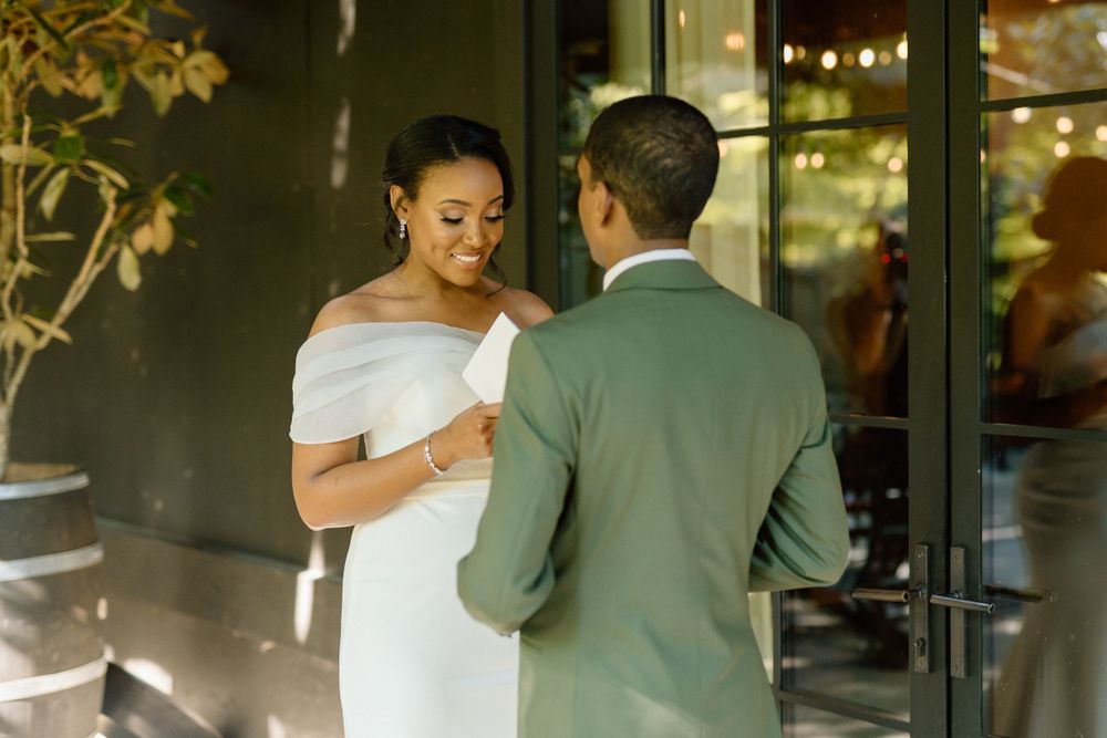 Couple shares romantic outdoor moment at sunset as bride in white dress holds wine glass near modern storefront.