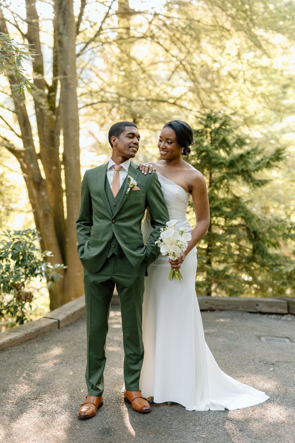 A wedding couple poses together on a wooded path bathed in golden sunlight.
