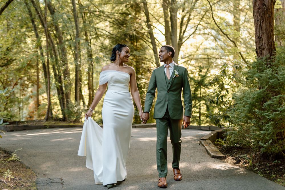 A couple in wedding attire walking down a tree-lined path on their special day, surrounded by lush greenery.