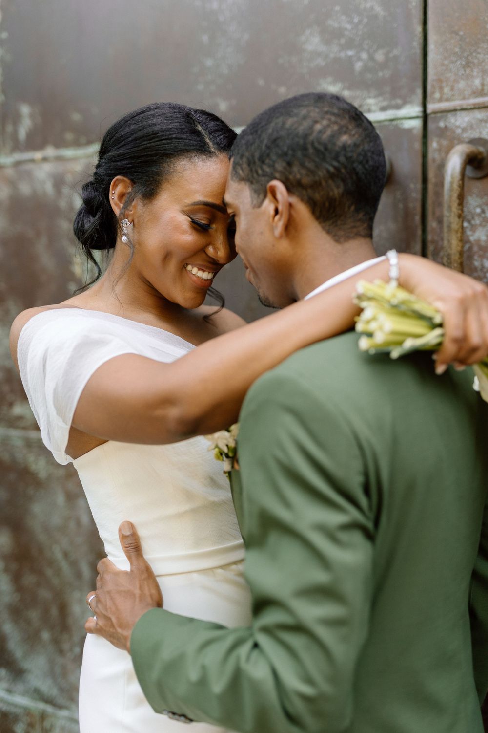 A tender moment shared between a couple on their wedding day, with the bride in white and groom in olive green attire.