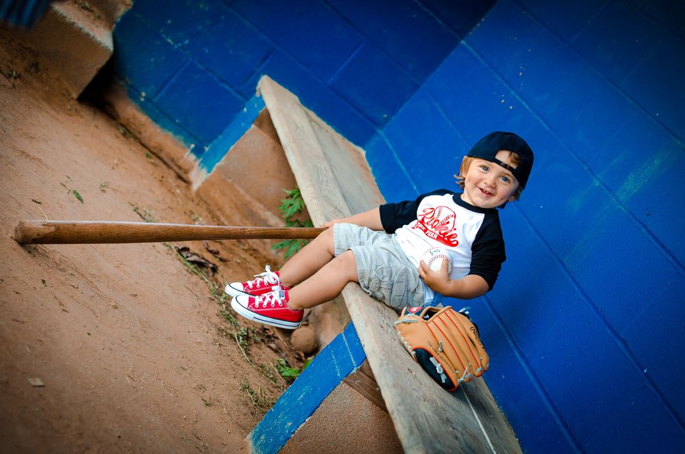 A person in casual attire sits on a concrete wall against a bright blue background wearing pink sneakers and a baseball cap.