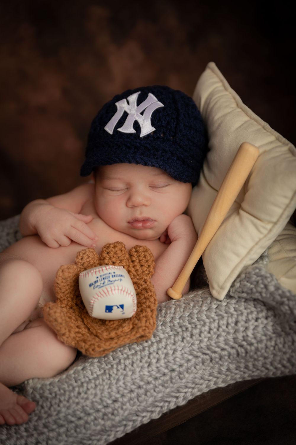 Sweet newborn photography with NY Yankees cap, baseball glove and bat on gray knit blanket.