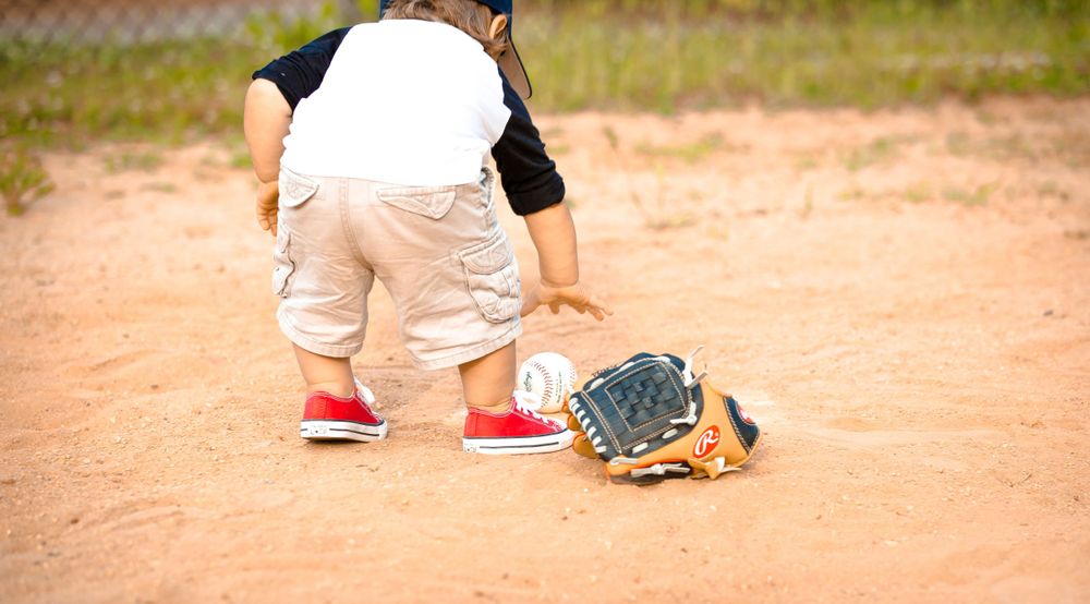 A player on a baseball field crouching with a baseball glove and bright red shoes on dirt ground.