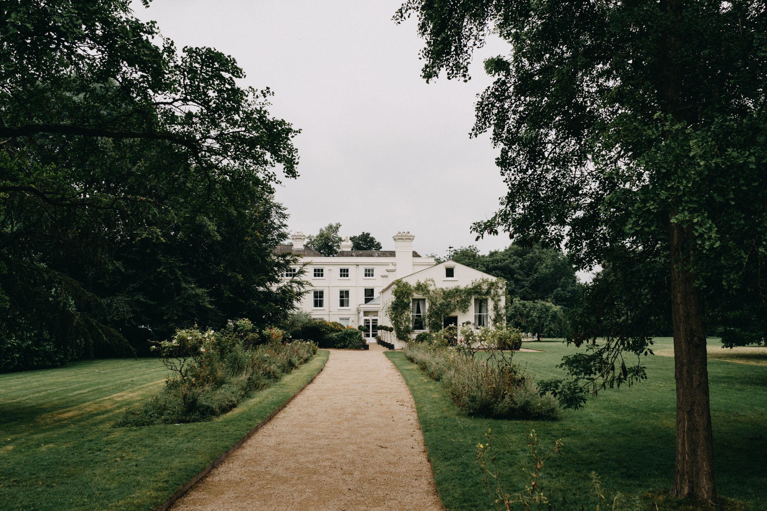 Morden Hall London, a grand white mansion with manicured gardens and a winding gravel path leading through lush green grounds.