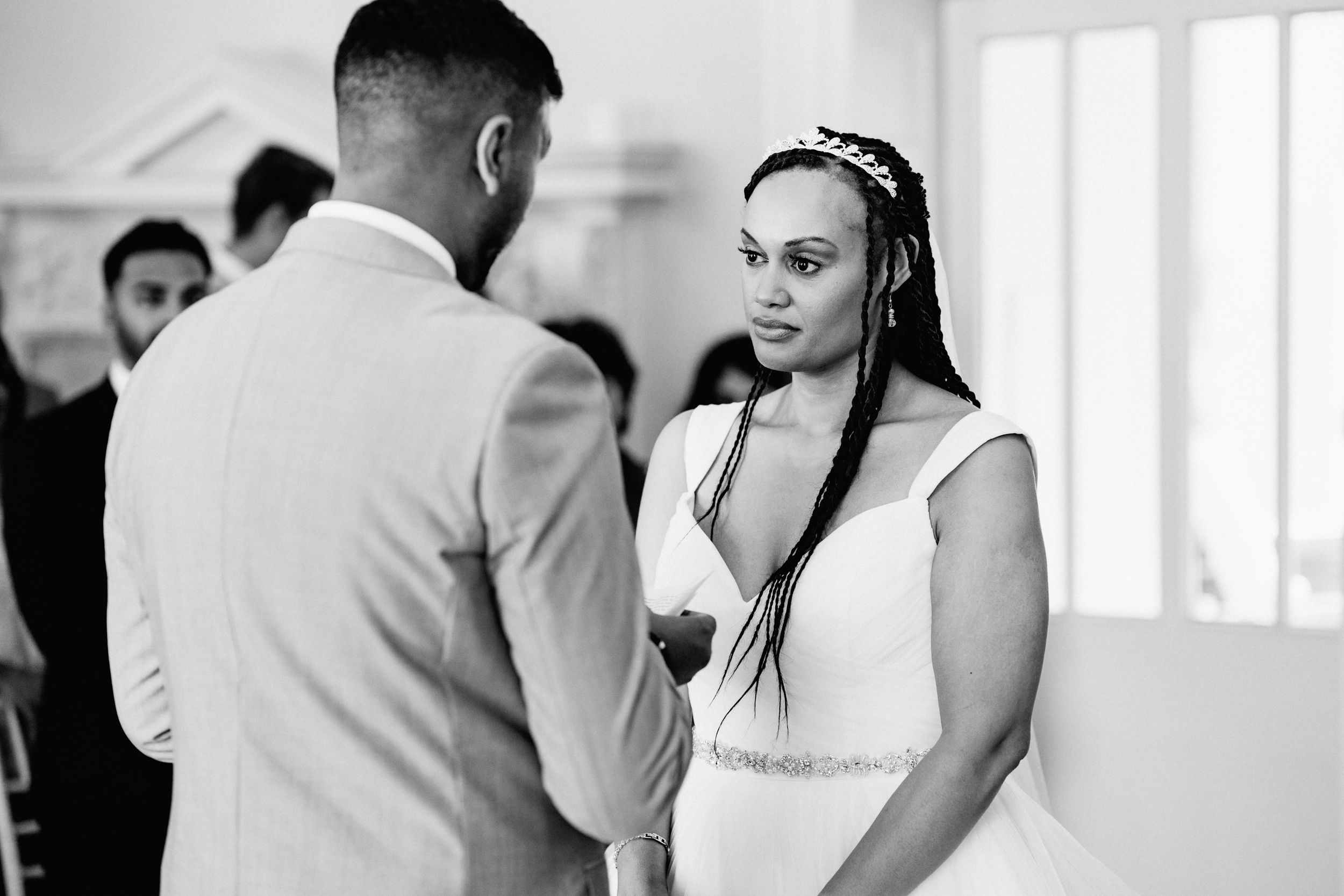 Black and white candid wedding photograph of bride during intimate ceremony moment in bright indoor setting.
