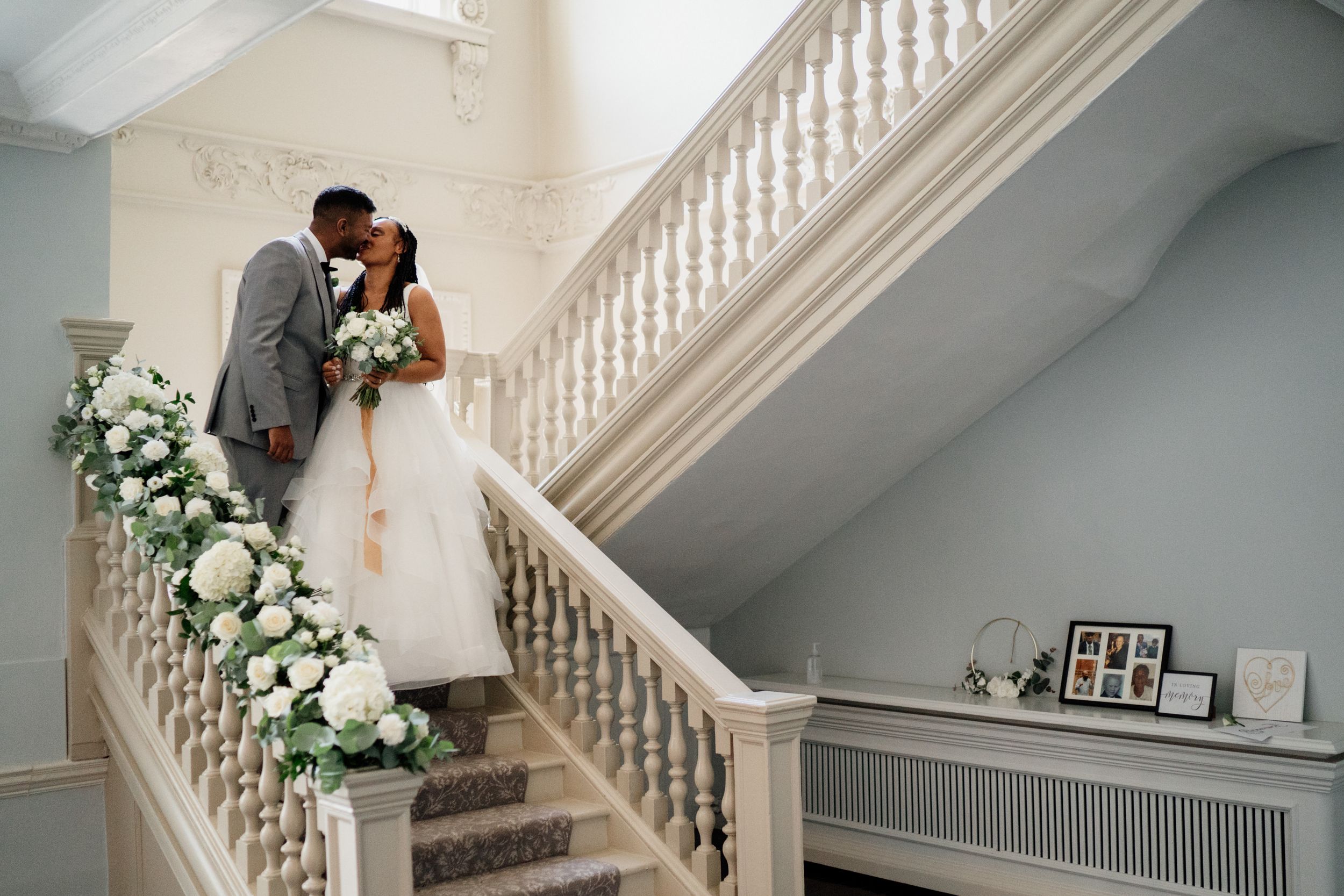 Elegant staircase decorated with white floral arrangements during a wedding ceremony at a mansion.
