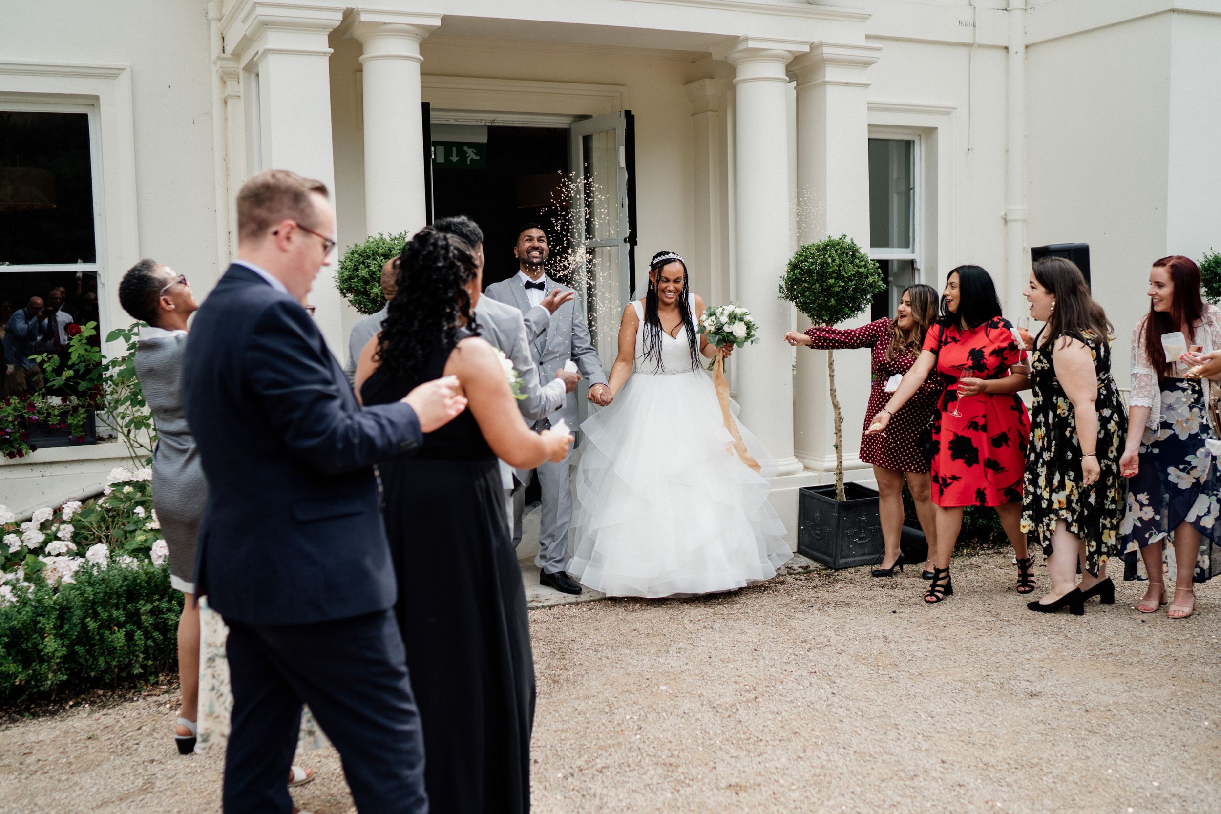 Wedding party gathered outside an elegant white columned venue entrance for an outdoor celebration ceremony.