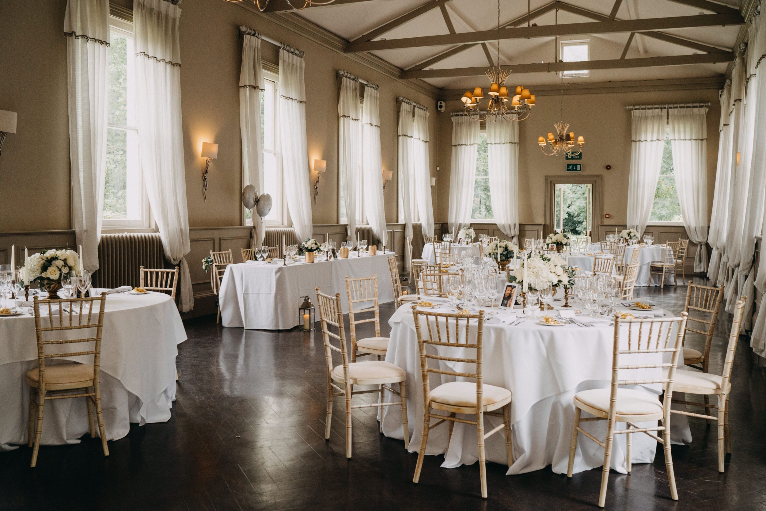 Elegant wedding reception venue with white linens, chiavari chairs, and classical chandeliers in a rustic-chic setting.