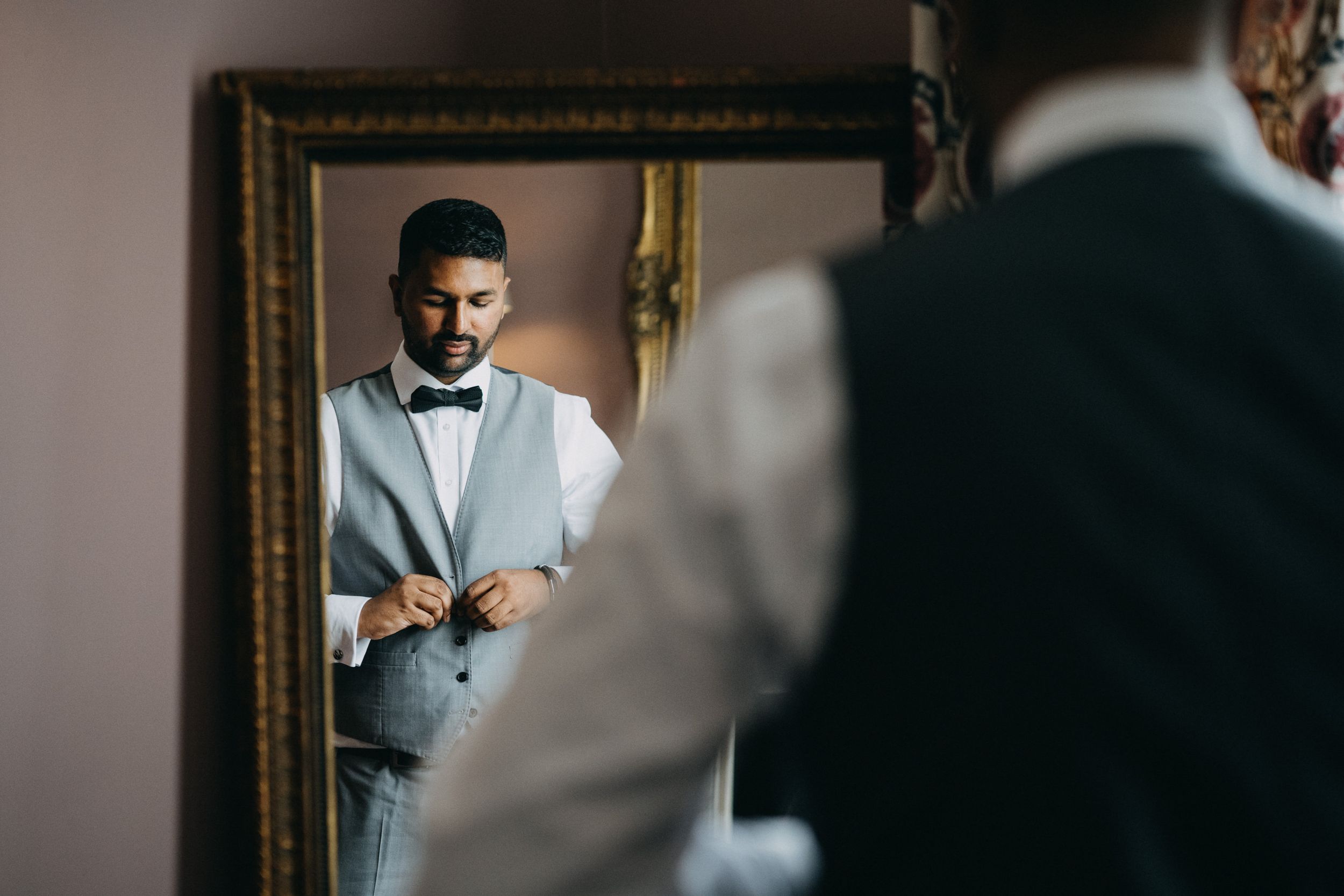 Mirror reflection shows someone wearing a light gray suit and black bow tie adjusting their cuffs.