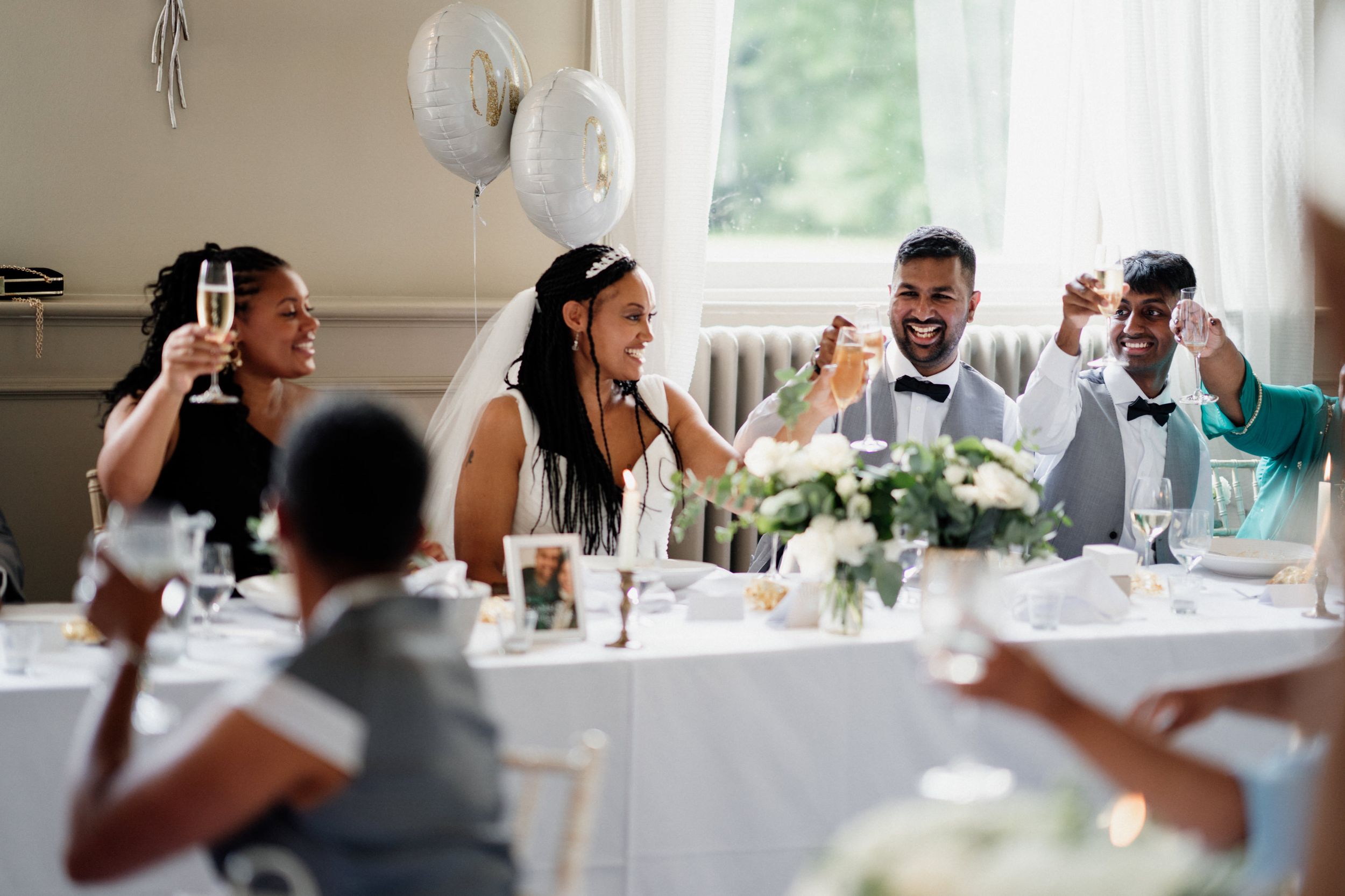Wedding guests share joyful laughter during a reception dinner at an elegant table with white linens and floral centerpieces.