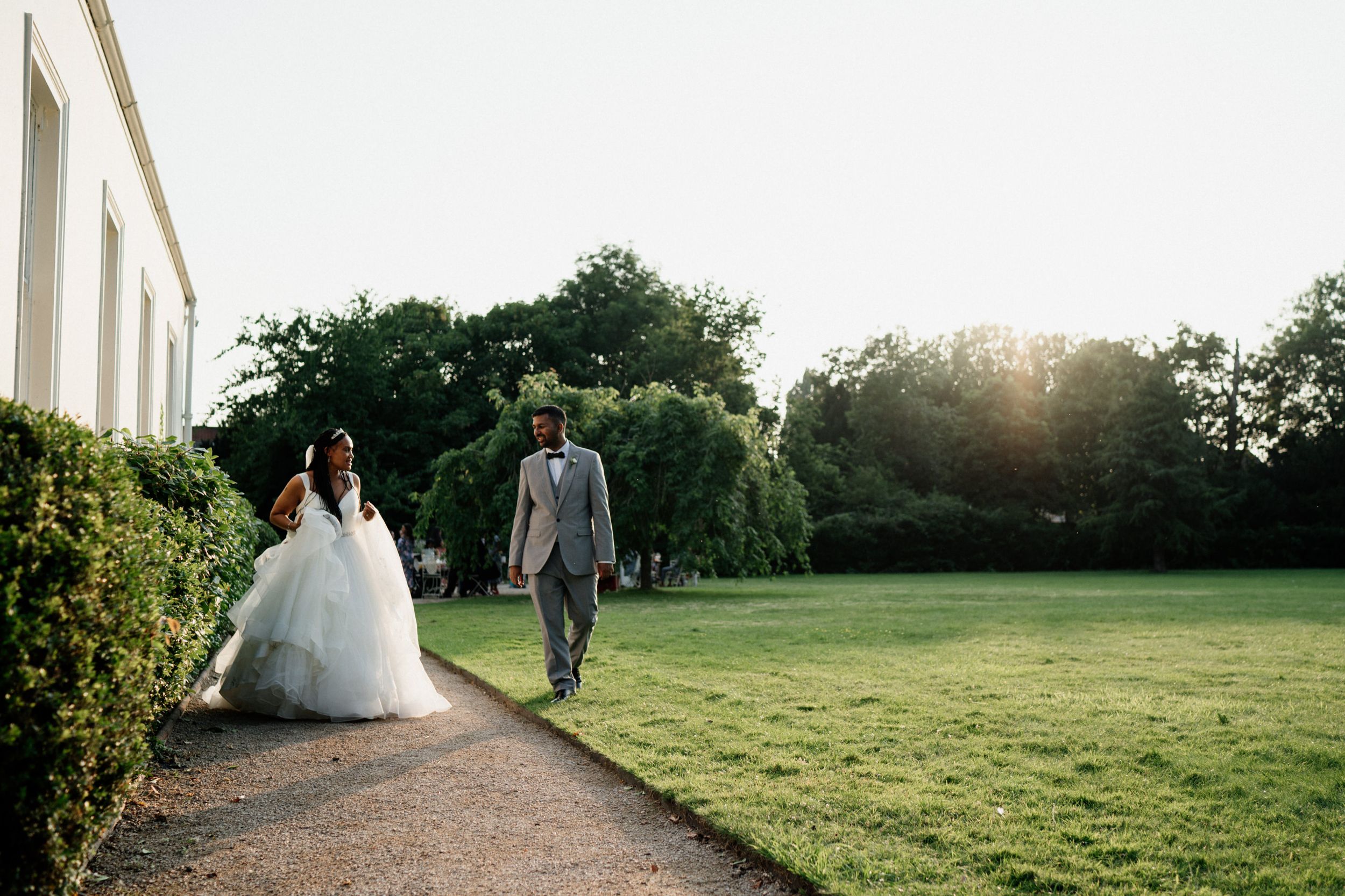 A couple strolls along a garden path during their wedding photoshoot at sunset.