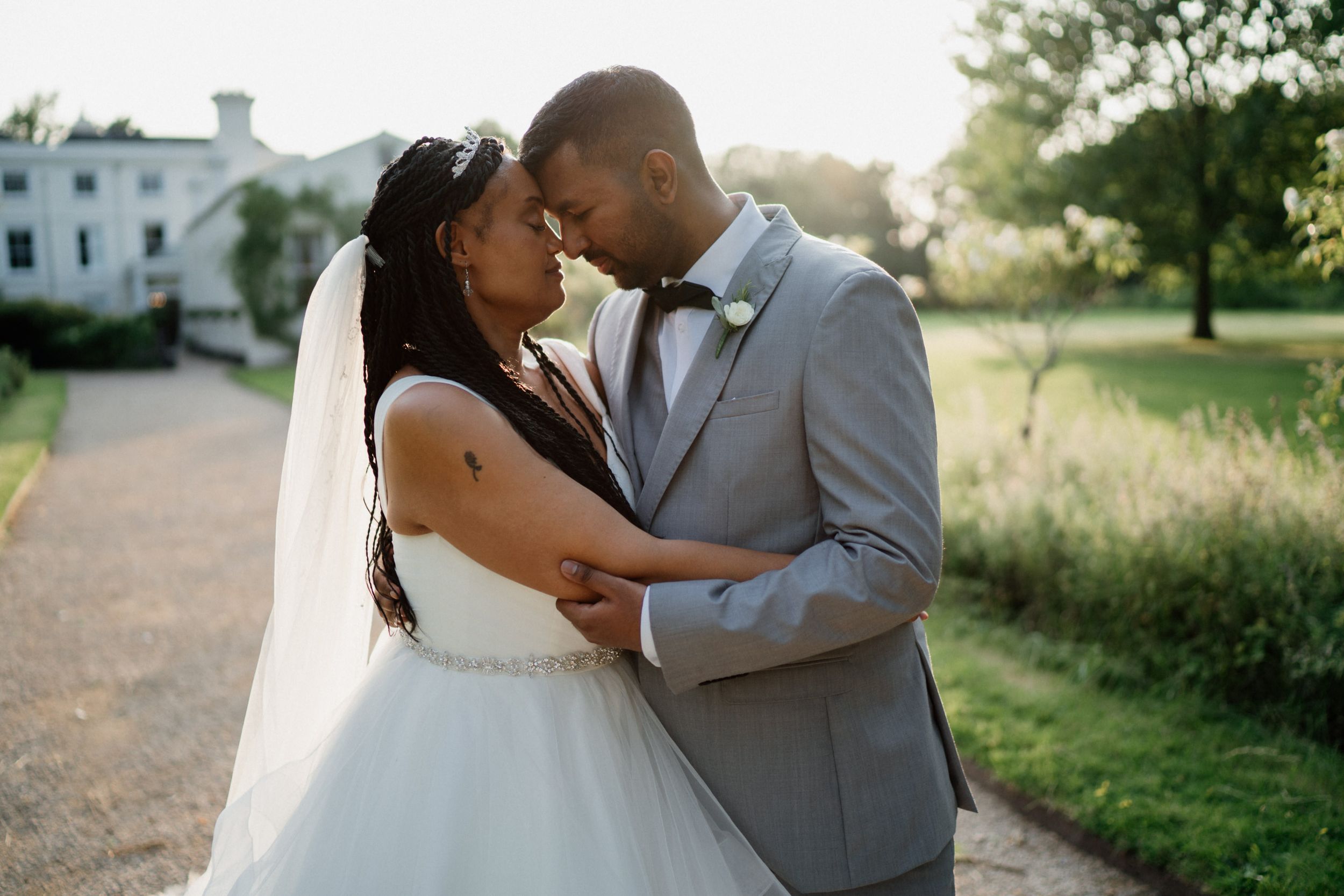A couple shares an intimate moment on their wedding day against a sunset backdrop wearing formal attire.